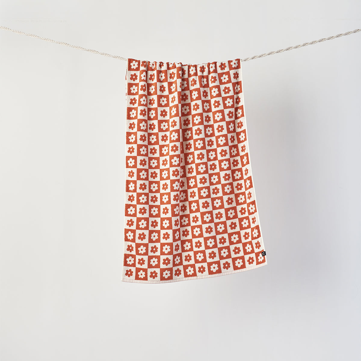 Bath towel, 100 cotton, red and white floral geometric pattern, hanging on a string.