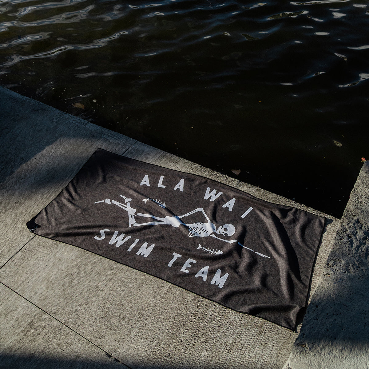 Black quick-drying towel with skeleton graphic by water’s edge.