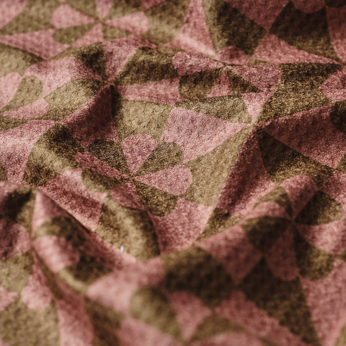Patchwork quilt in brown and pink with geometric and floral patterns, textured fabric.