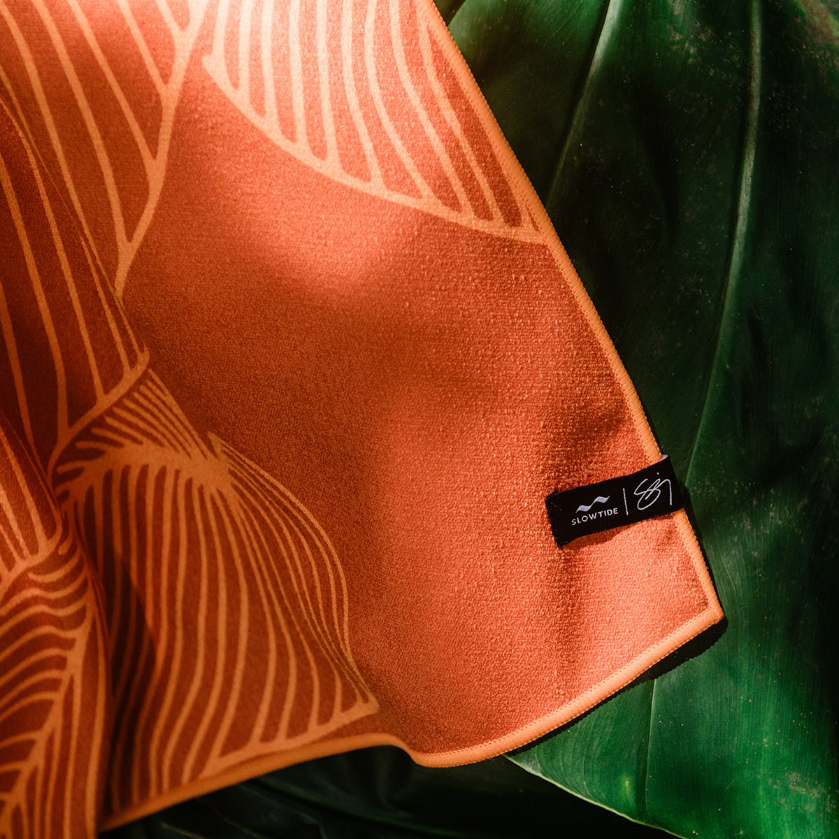 Towel with orange leaf pattern, displayed on large green leaves.