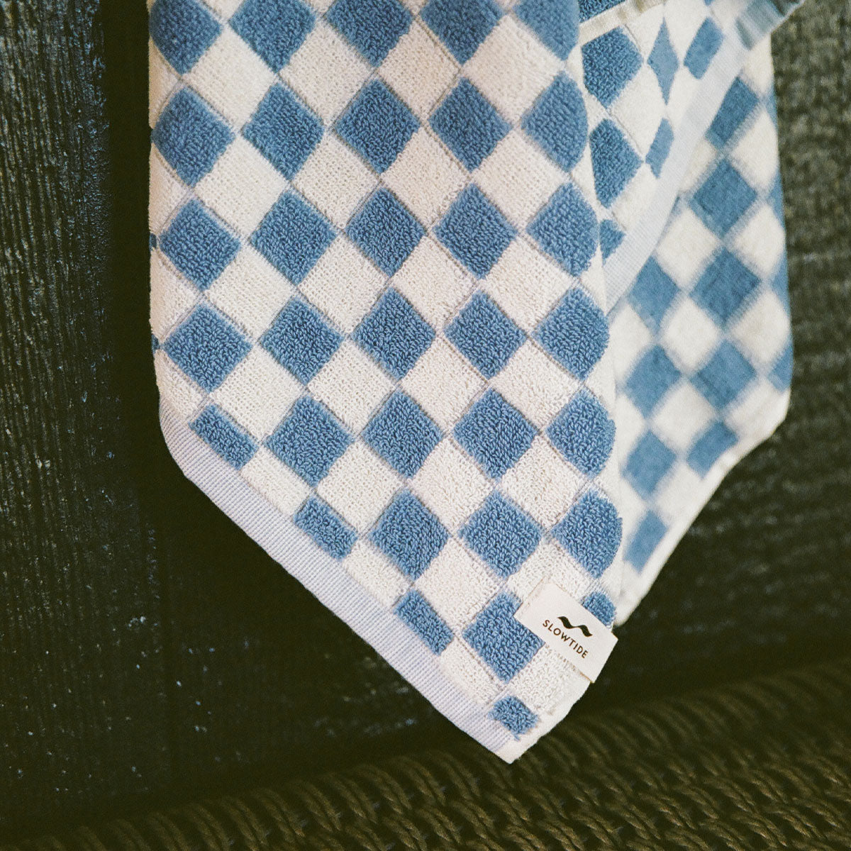 Cotton terry bath towel with blue and white checkerboard pattern on dark surface.