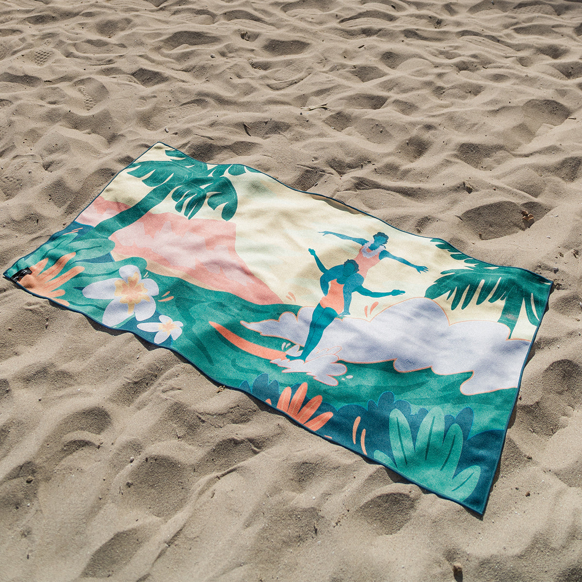 Quick-drying towel with colorful surfing design on sand.