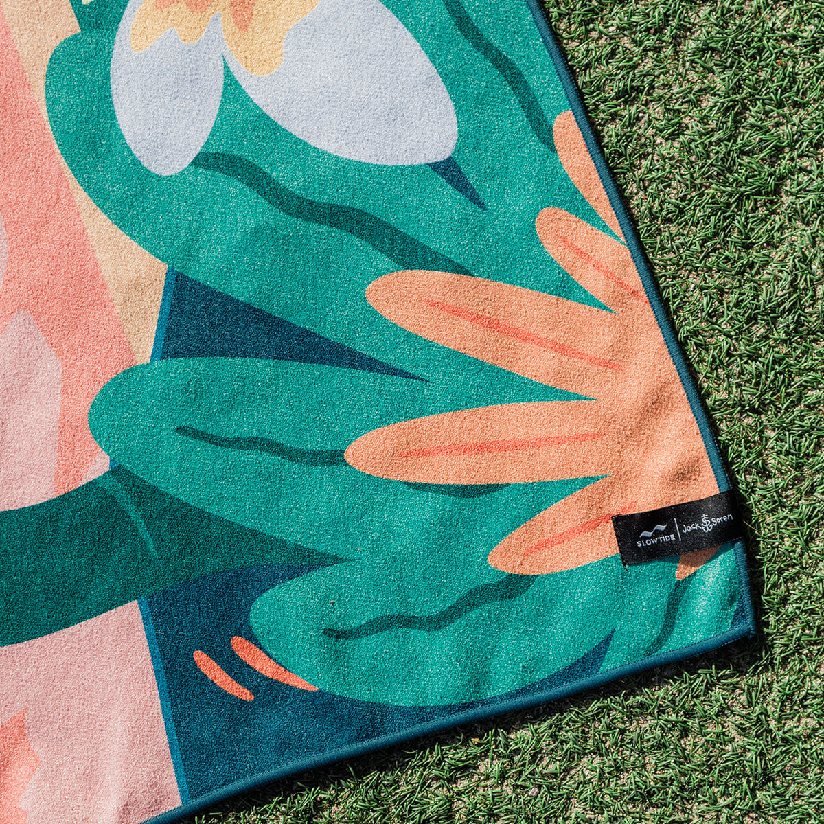 Quick-drying sustainable towel with abstract leaf pattern, shown outdoors on grass.