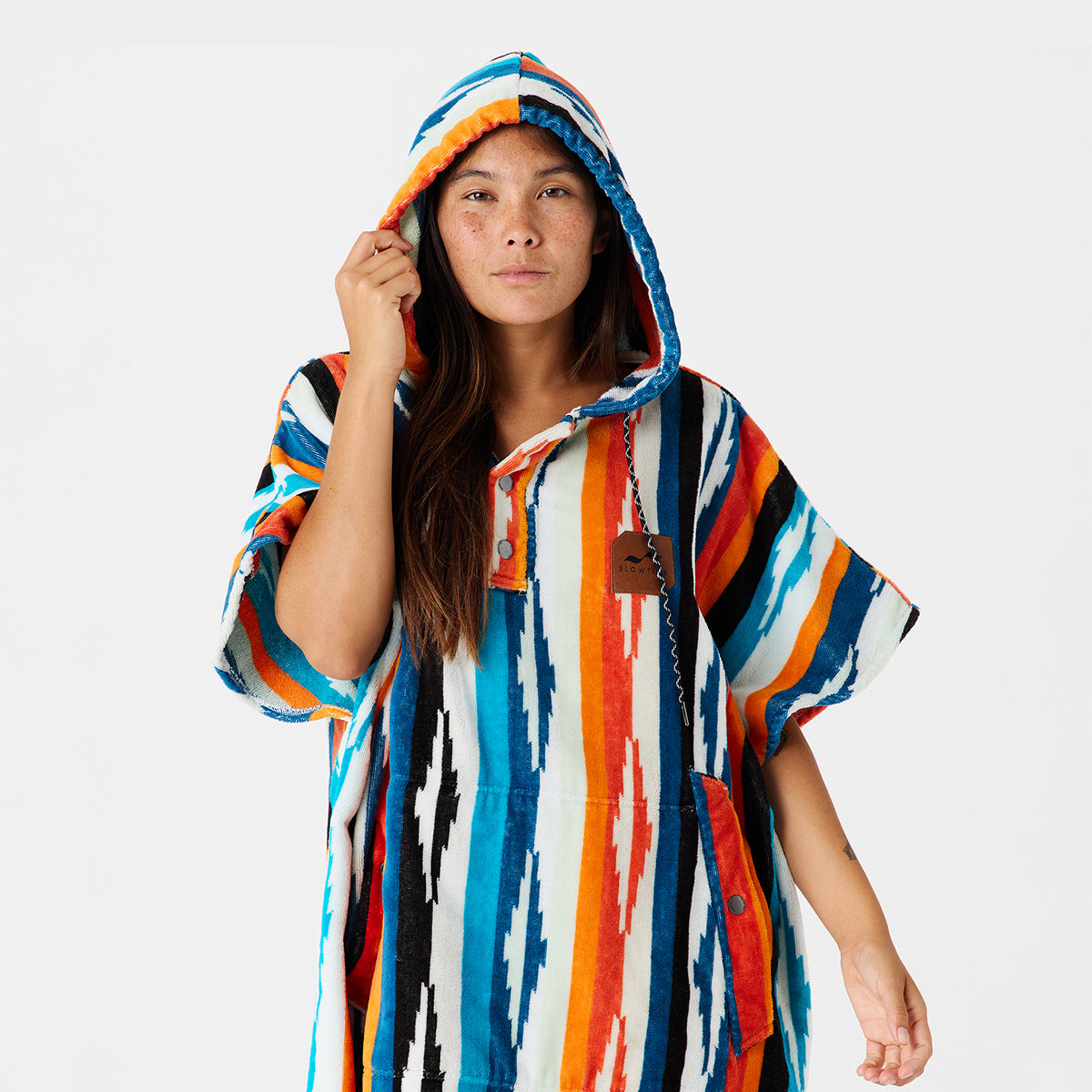 Towel poncho in soft cotton terry with colorful patterns and hood on plain background.