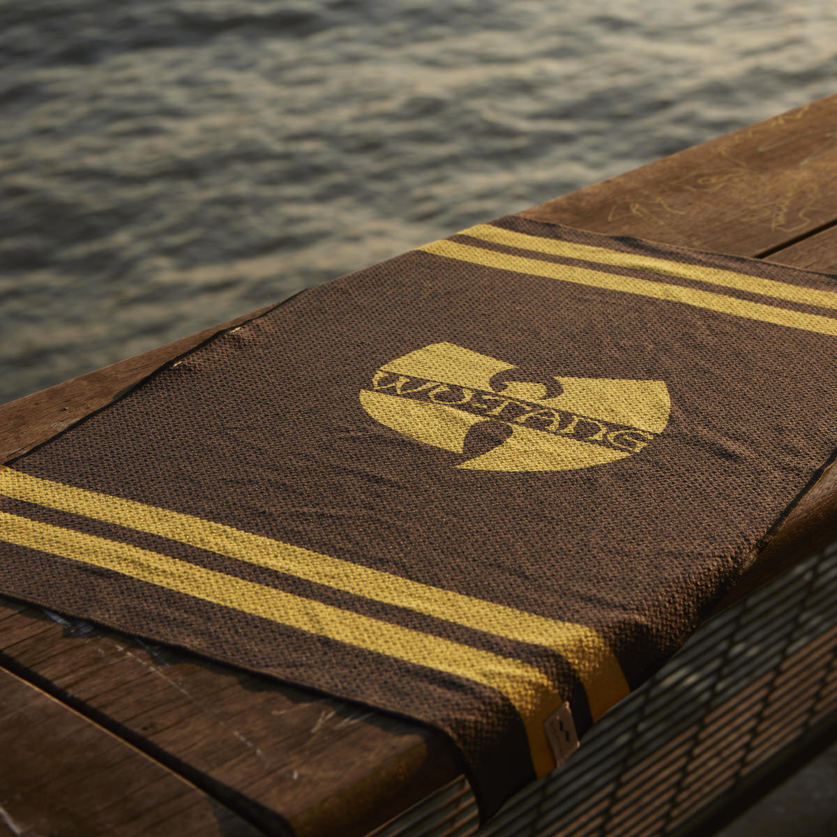 Brown eco-friendly kitchen towel with yellow stripes and logo, displayed on wood outdoors.