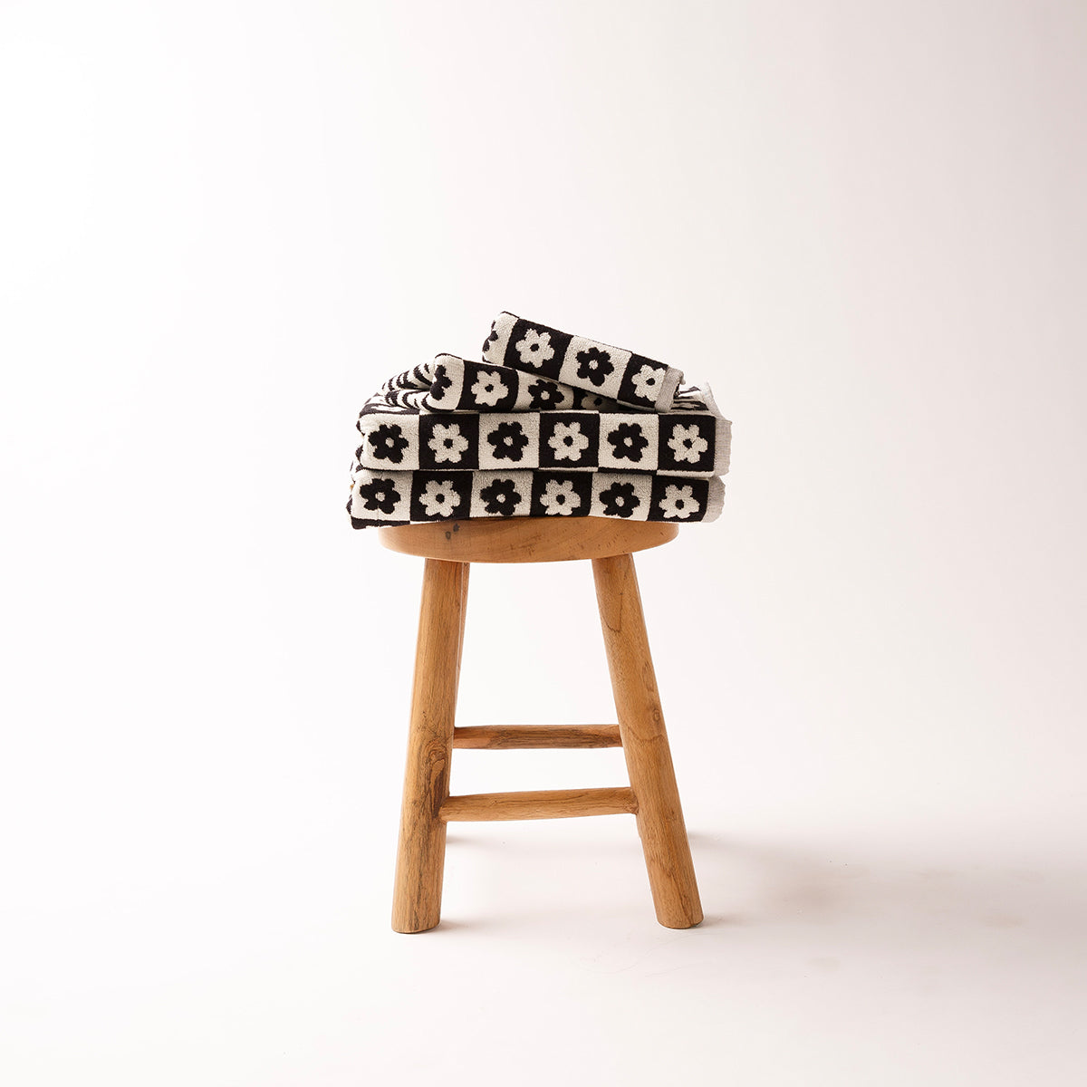 Bath towel with black and white floral pattern, folded on a wooden stool.