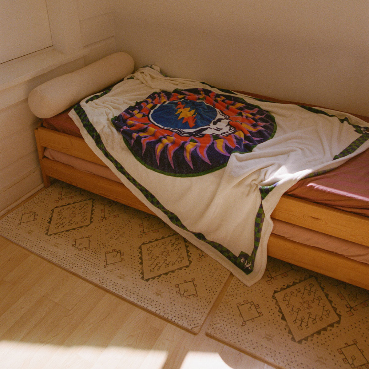 Single bed with oversized recycled polyester blanket, patterned rugs on wooden floor.