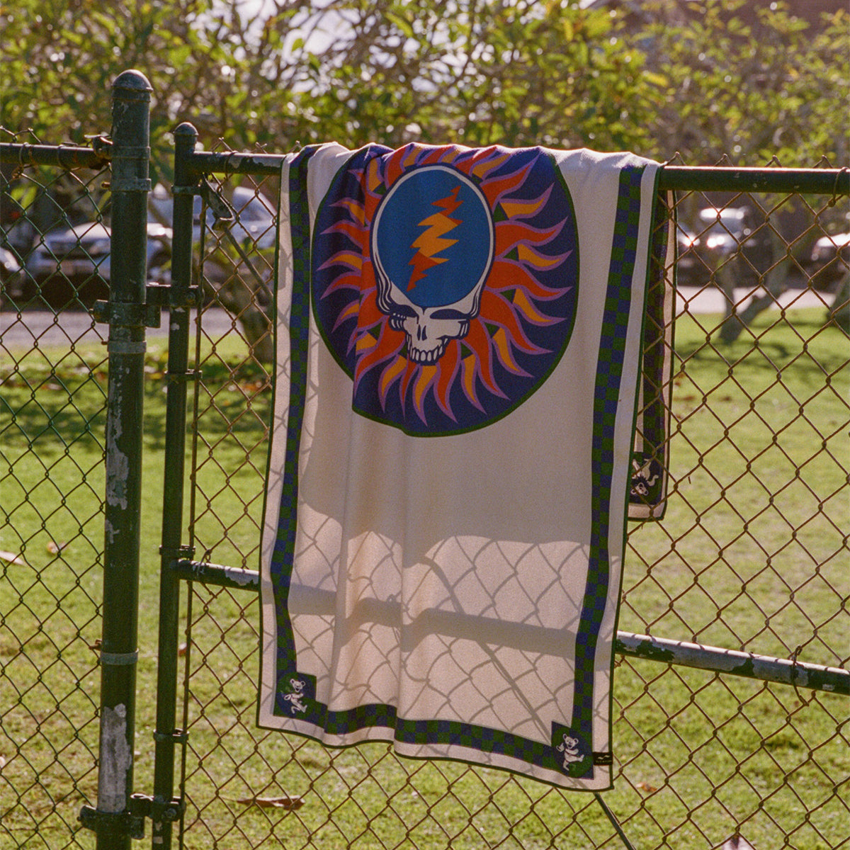 Sustainable towel with skull and lightning bolt print, displayed on a fence outdoors.