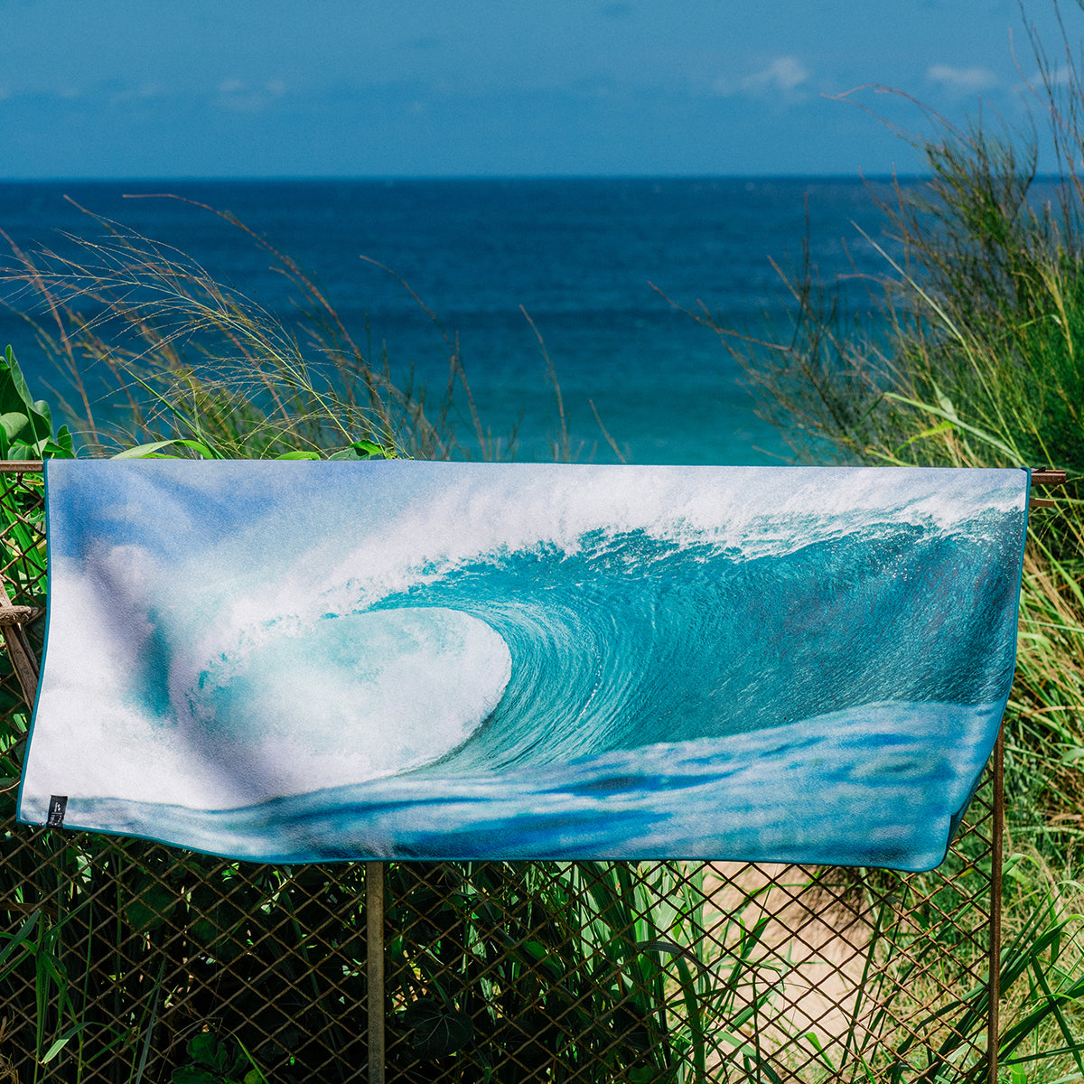 Quick-drying towel with wave print hanging on a fence near the ocean.