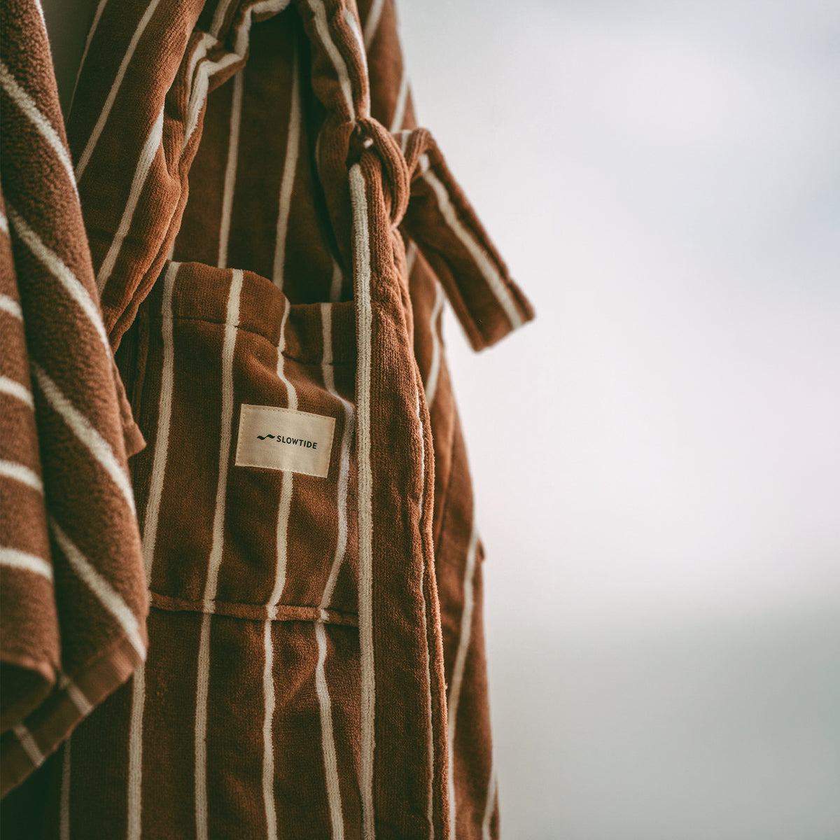 Hooded robe in plush brown and white stripes with a waist tie and patch pocket.