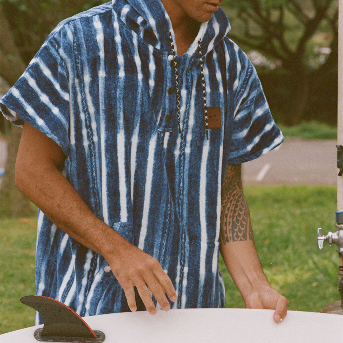 Cotton poncho with blue stripes, absorbent design, shown near a surfboard outdoors.