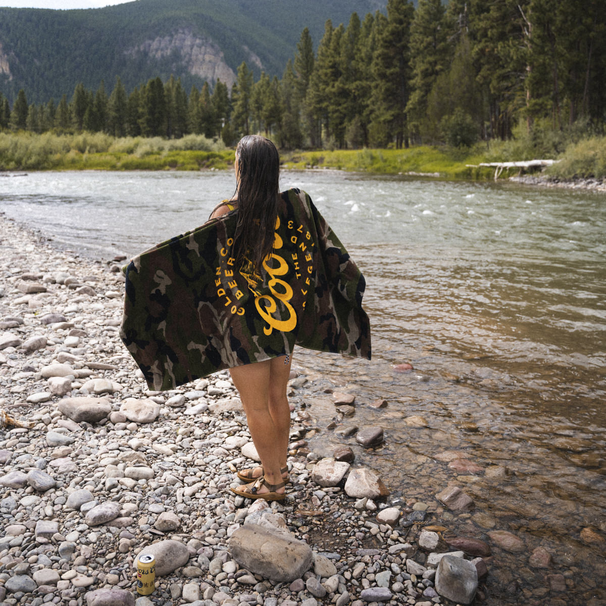 Printed beach towel with vibrant pattern on rocky riverbank outdoors.