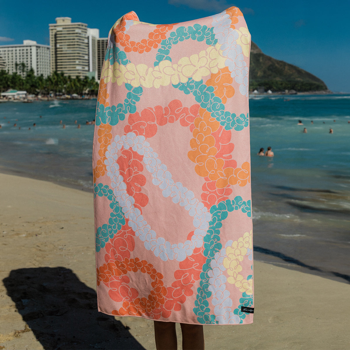 Recycled plastic beach towel with colorful pattern on sand.