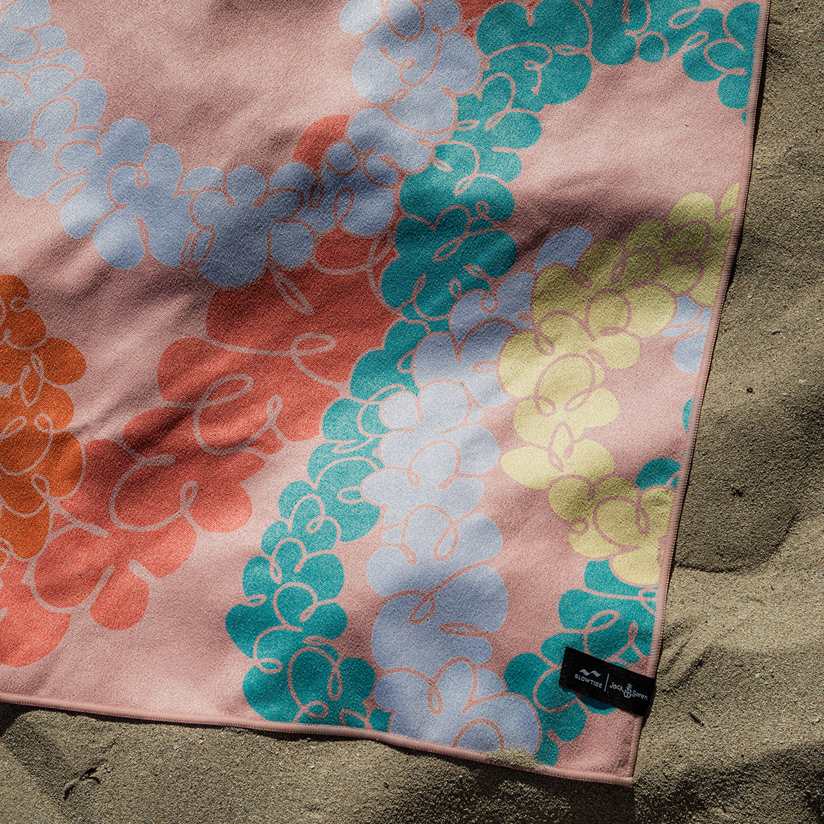 Travel towel with floral pattern, quick-dry fabric, shown on sand in natural light.