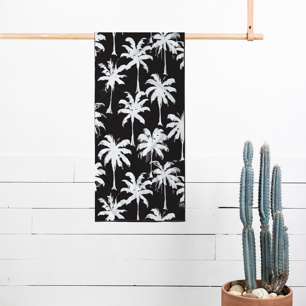 Recycled quick-dry towel with white palm tree print hanging by cactus and rocks.