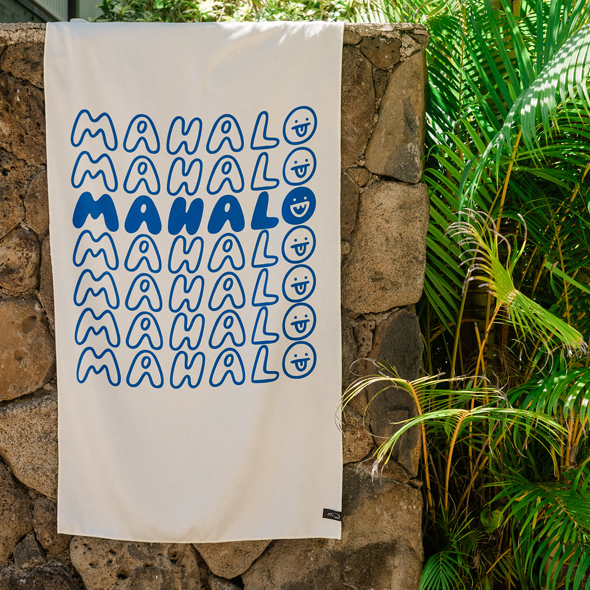 Quick-drying recycled towel with blue text and smiley face pattern hanging near plants.