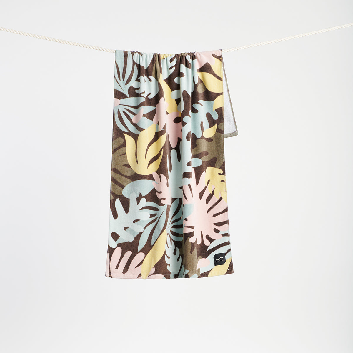 Velour towel with tropical print, absorbent cotton finish, shown hanging on a rope.