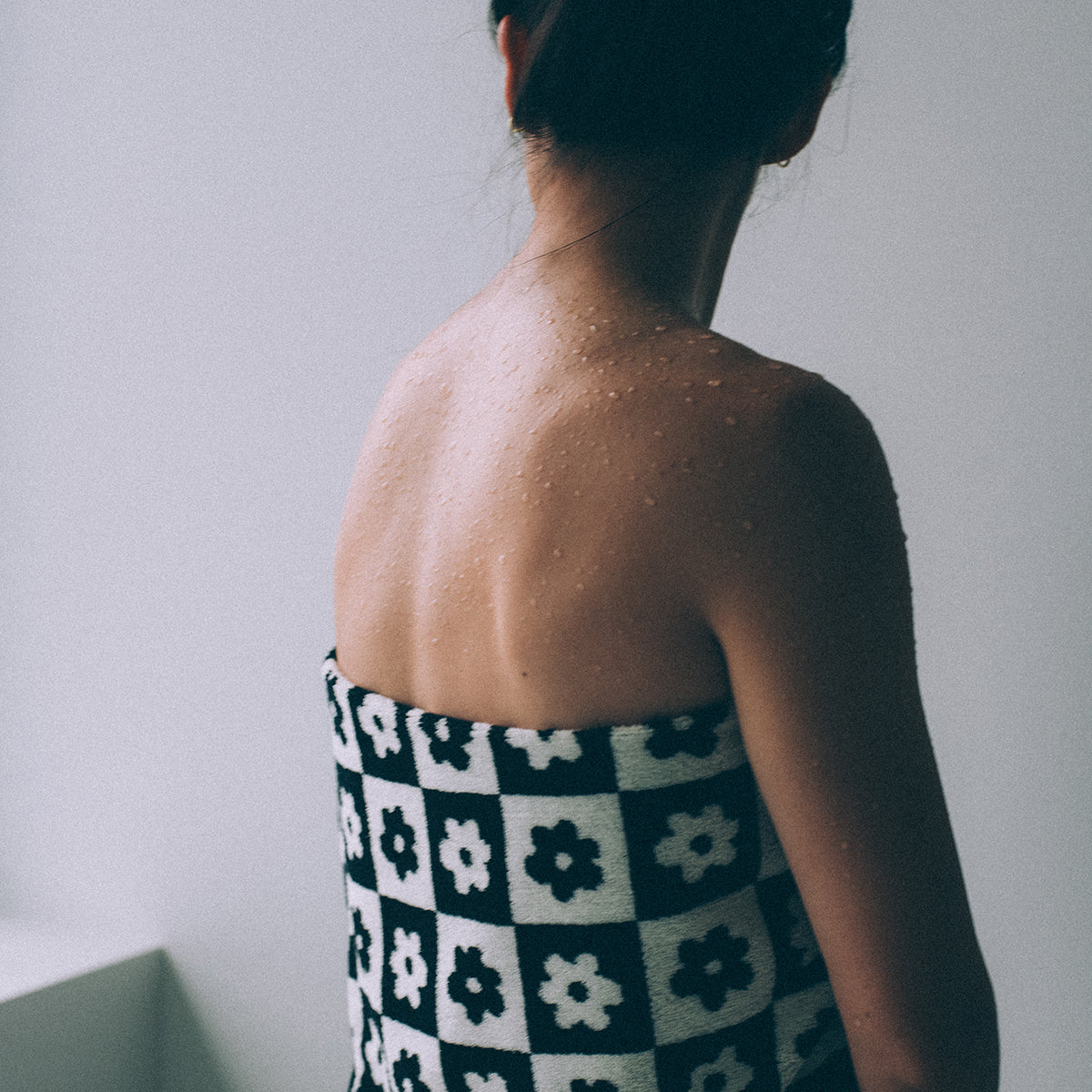 Bath towel with black and floral pattern, shown wrapped around wet shoulders.