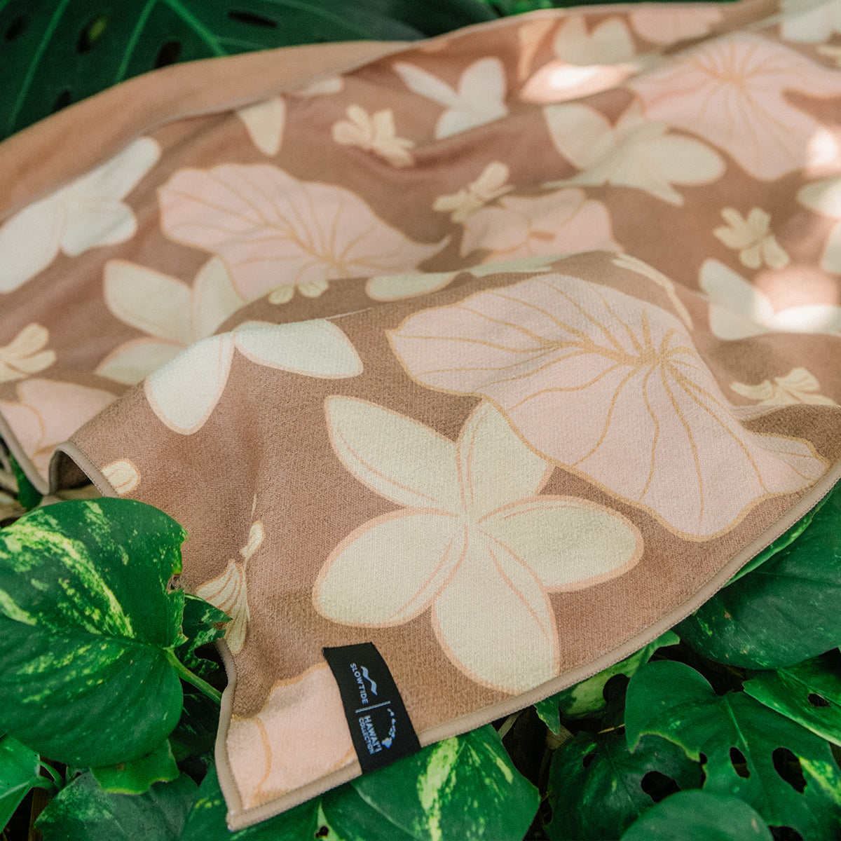 Quick-drying beige towel with floral pattern on green tropical leaves.