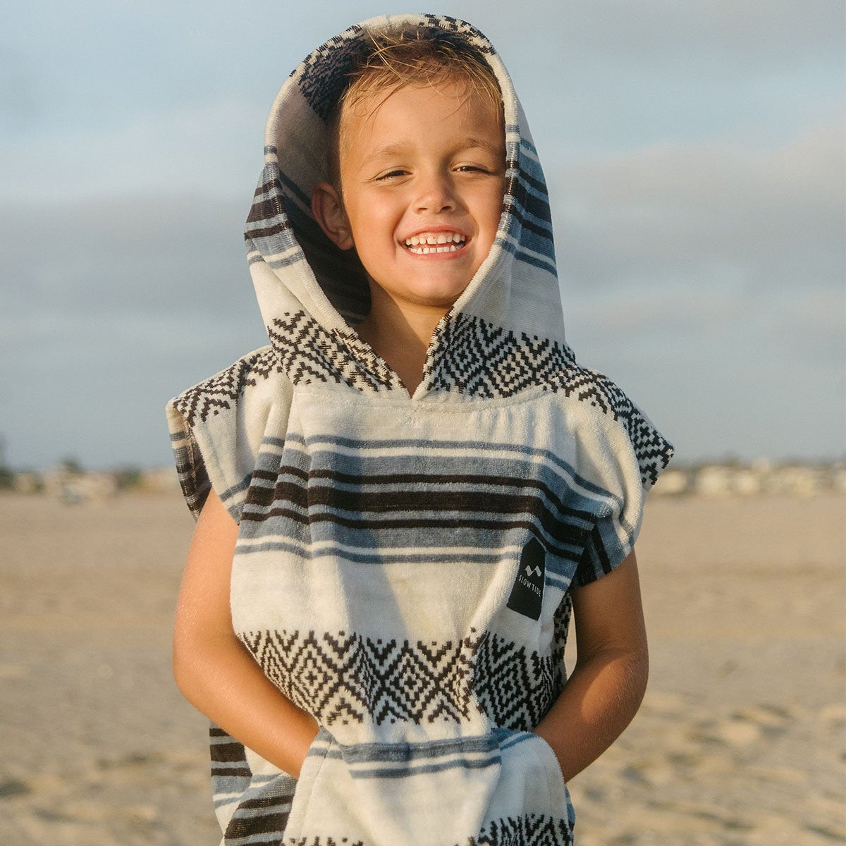 Hooded poncho towel in cotton terry with a blue, black, and white geometric stripe pattern.
