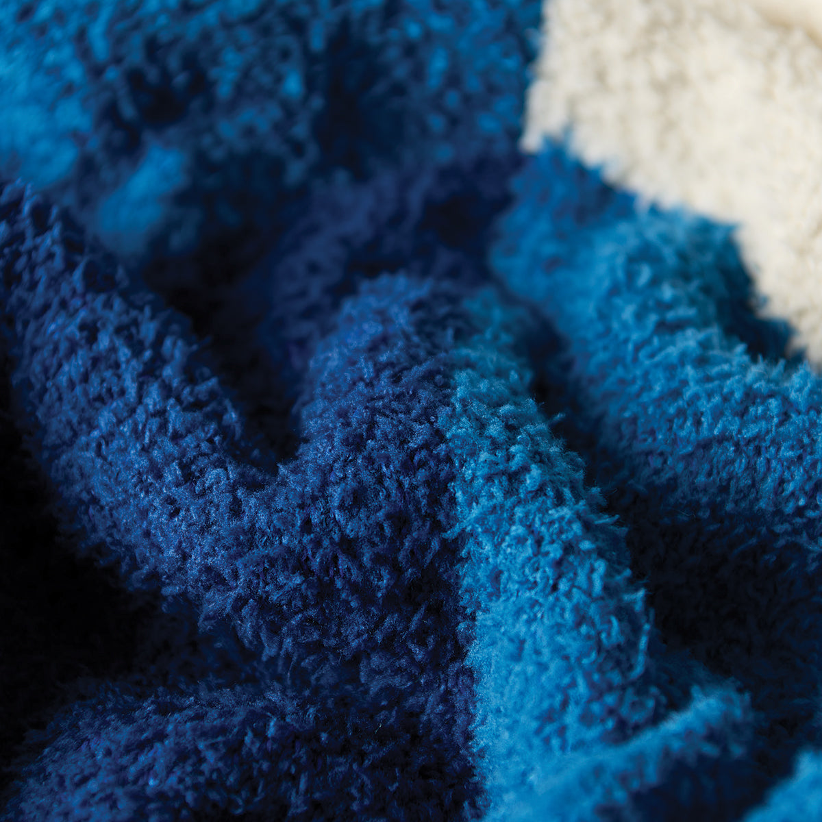 Reversible plush throw blanket with blue and cream color-blocked pattern.