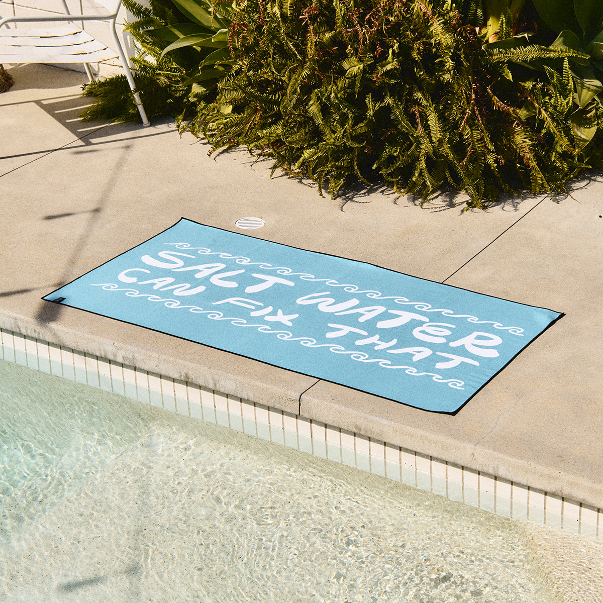 Blue quick-dry towel with Salt water can fix that text, shown poolside.