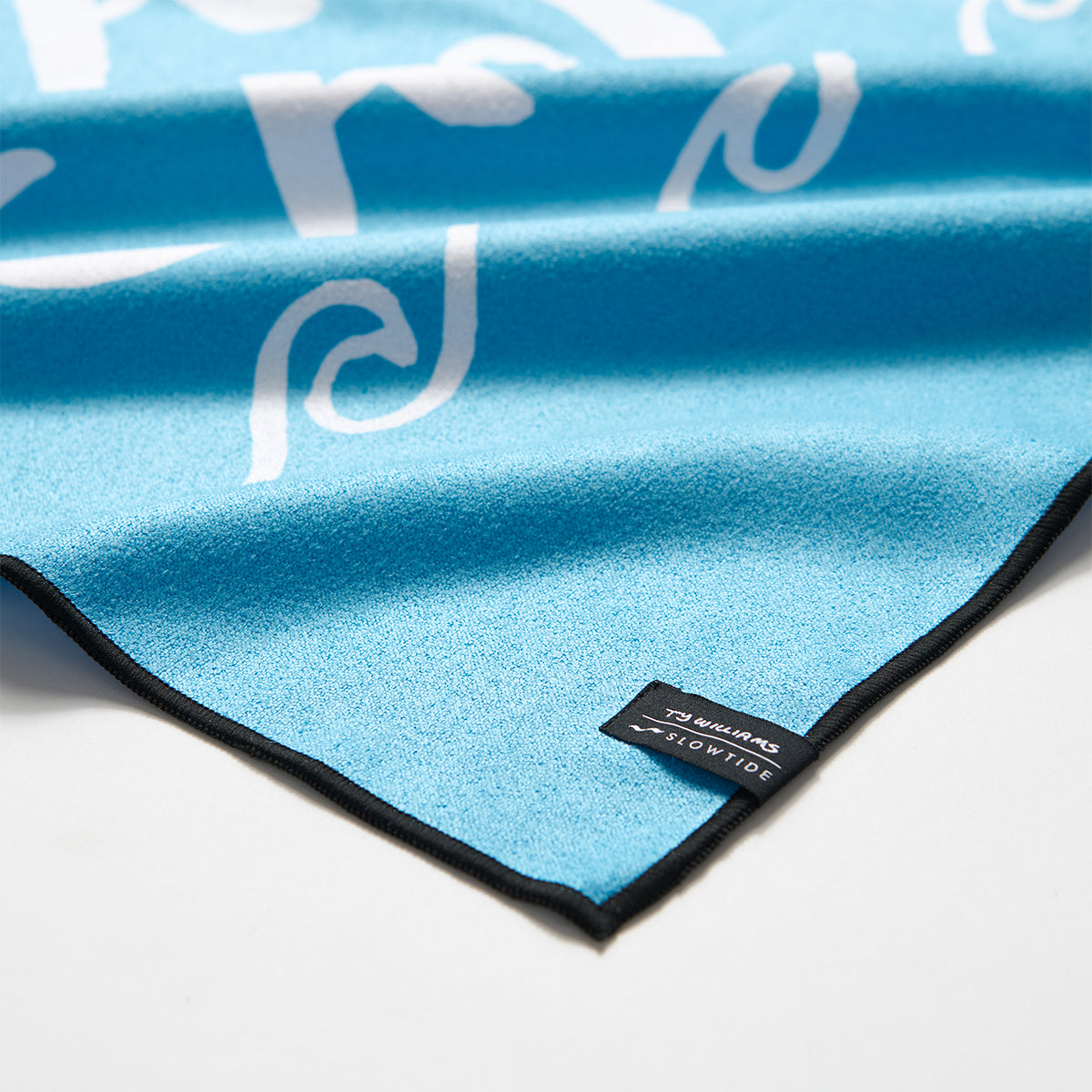 Blue absorbent towel with white pattern, black trim, and small black fabric tag.