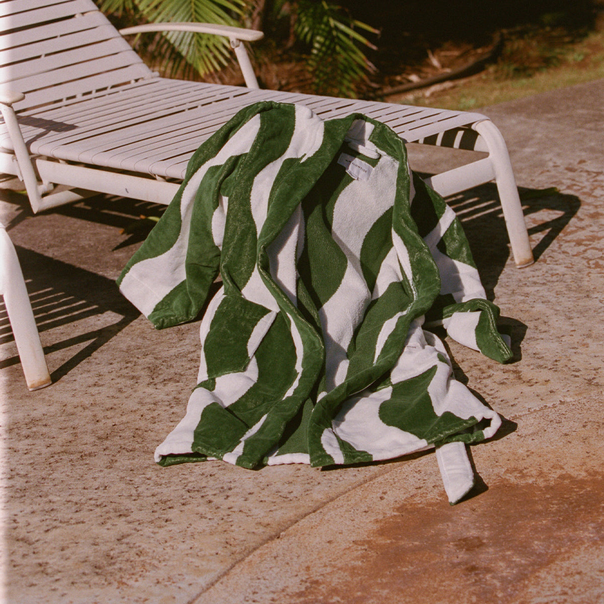 Bathrobe displayed on a white poolside lounge chair in sunlight.