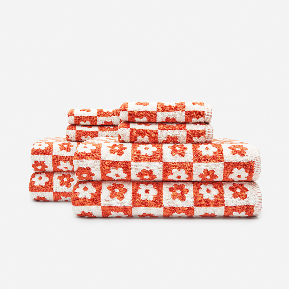 Floral bath towels, cotton, red and white checkerboard pattern, stacked on plain background.