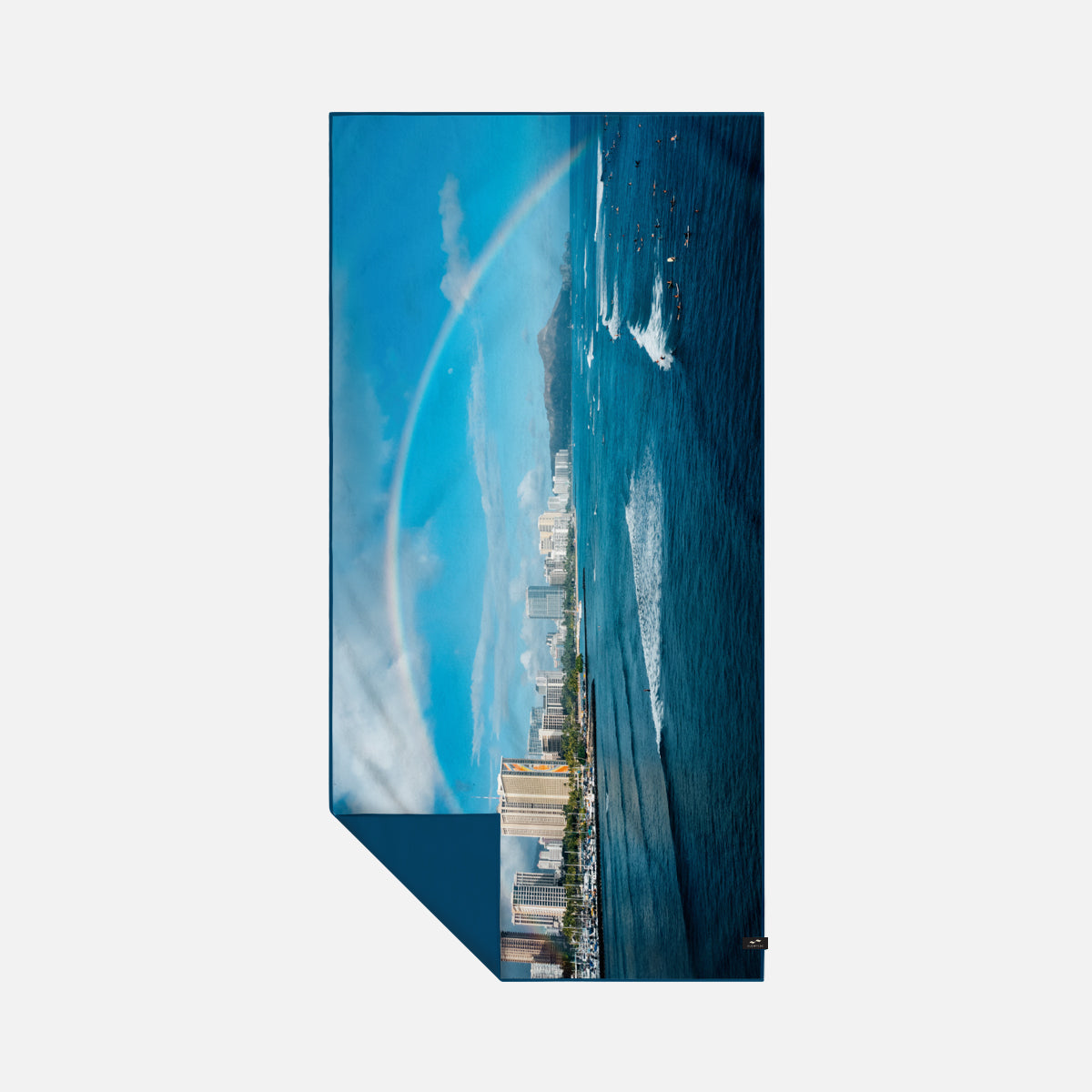 Sustainable towel on ocean shore with city skyline and rainbow in background.