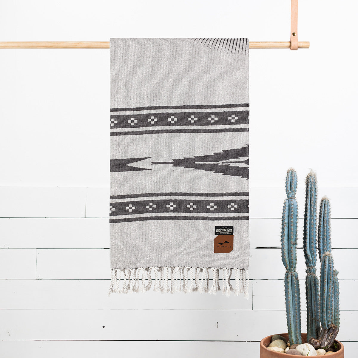 Beach blanket with geometric pattern and fringed hem, displayed on wooden bar.