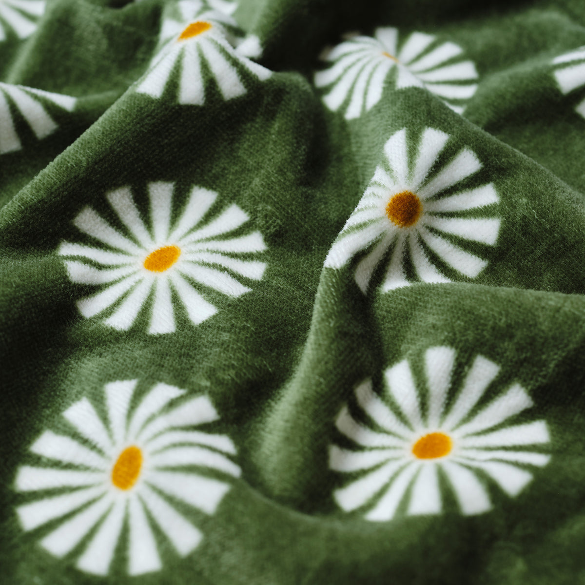Cotton towel in green with white daisies and yellow centers, slightly wrinkled.