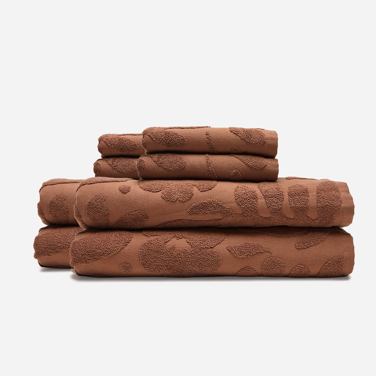 Brown cotton bath towels with subtle botanical print, stacked on white background.
