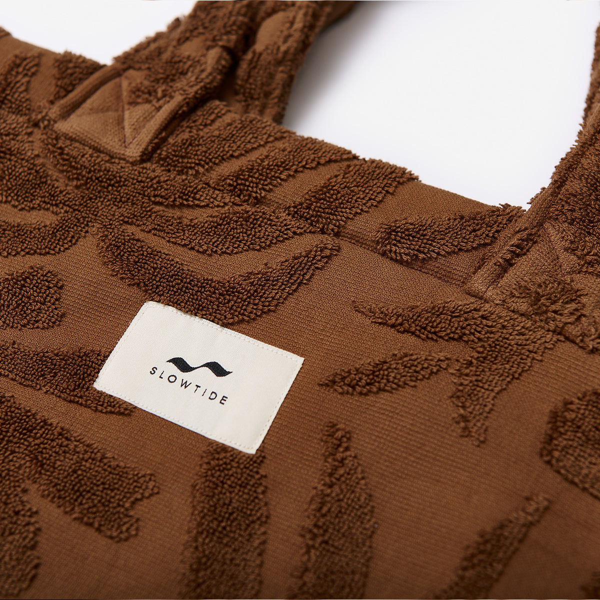 Tote bag in brown cotton canvas with white label and botanical print, shown on display.