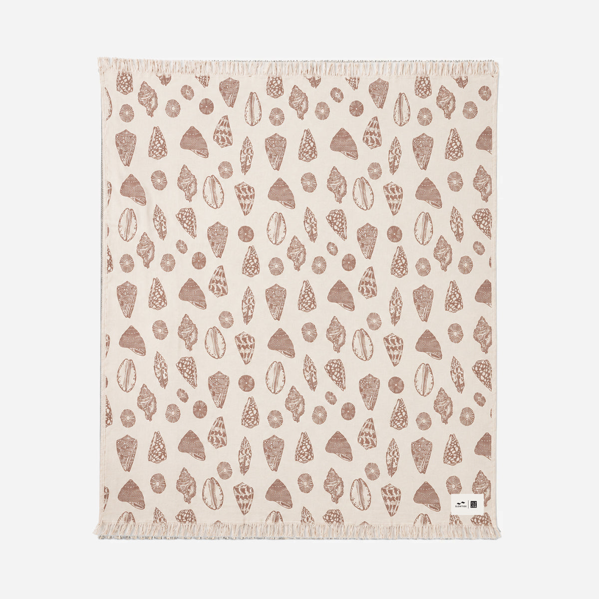 Beige oversized blanket with brown shell and rock pattern, fringed edges, small white tag.