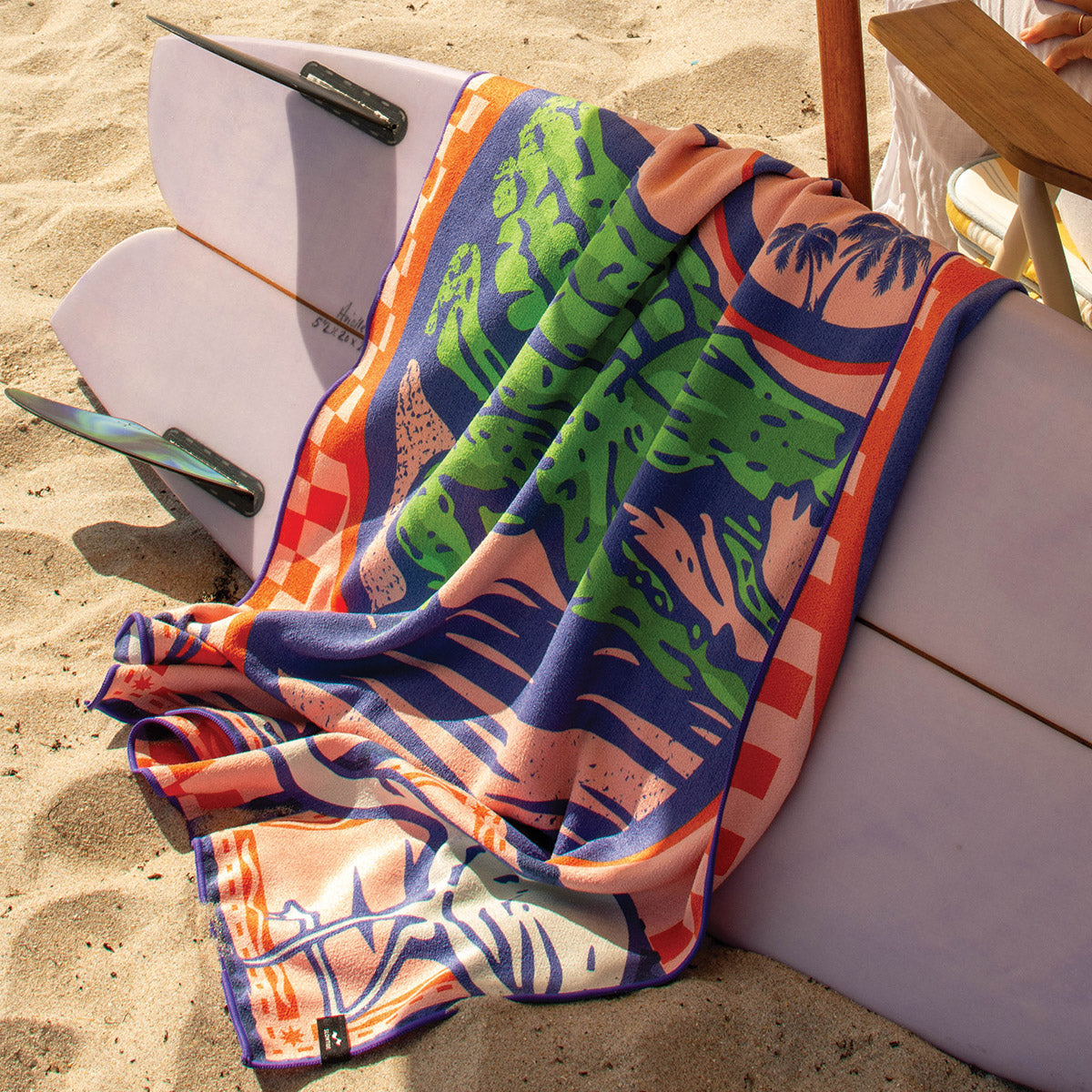Quick-drying travel towel with soft texture displayed on a surfboard at the beach.