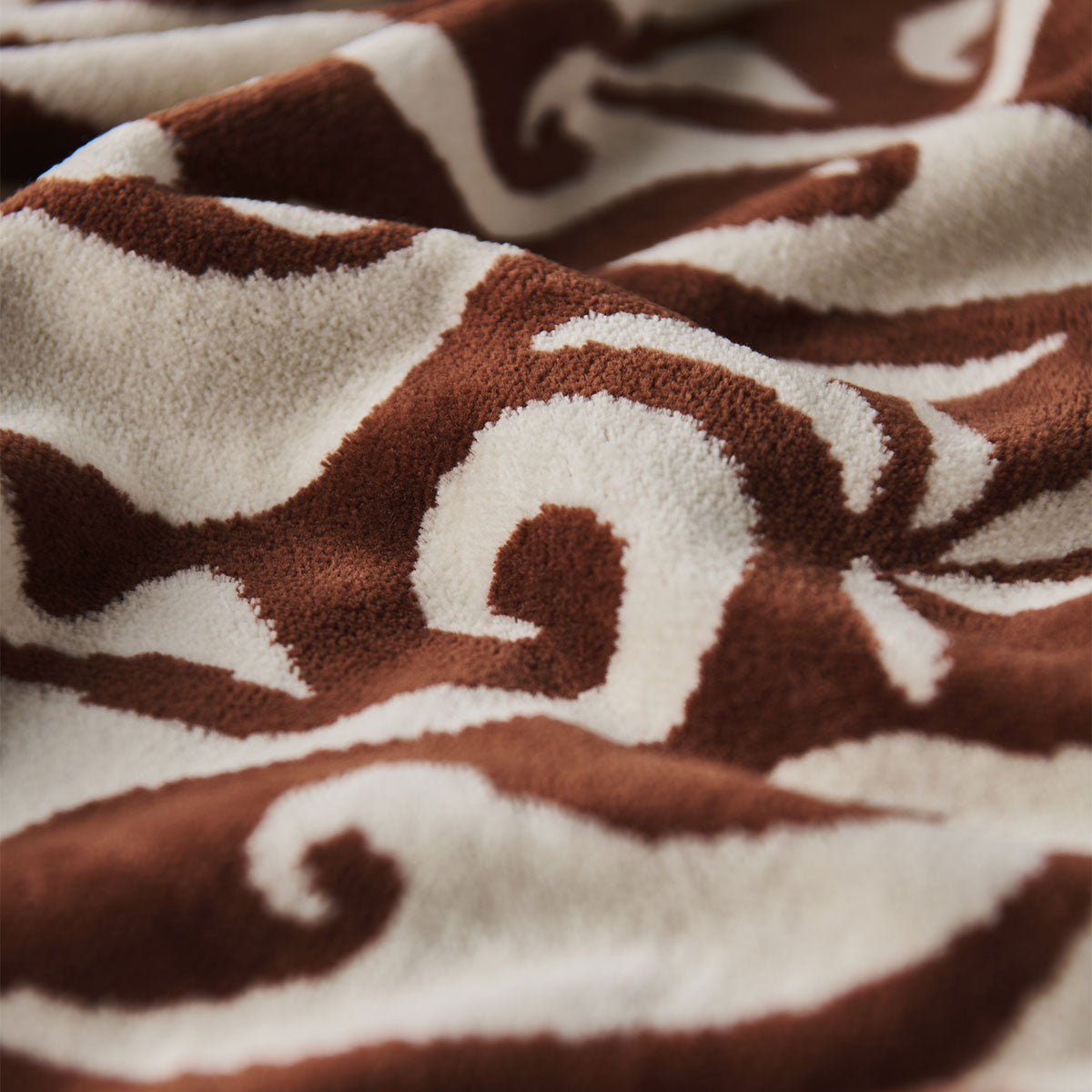 Fleece blanket with warm rust wave pattern on soft brown and white, vintage textile look.