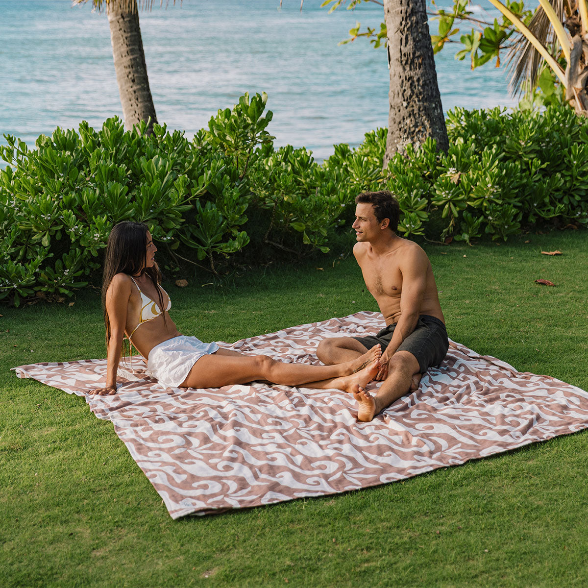 Oversized sand-resistant beach blanket with a tan and white wave pattern on grass.