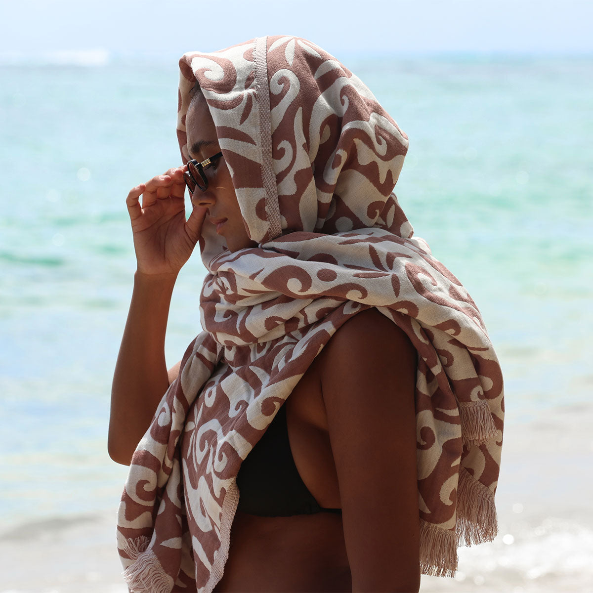 Patterned shawl with wave print towel placed on sandy beach.