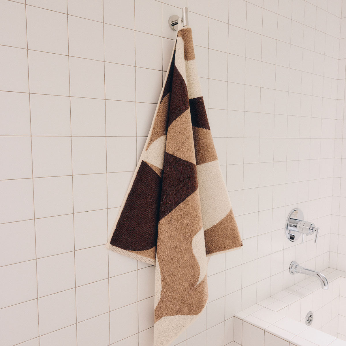 Quick dry bath towel in a brown and tan geometric pattern hanging on a tiled wall.