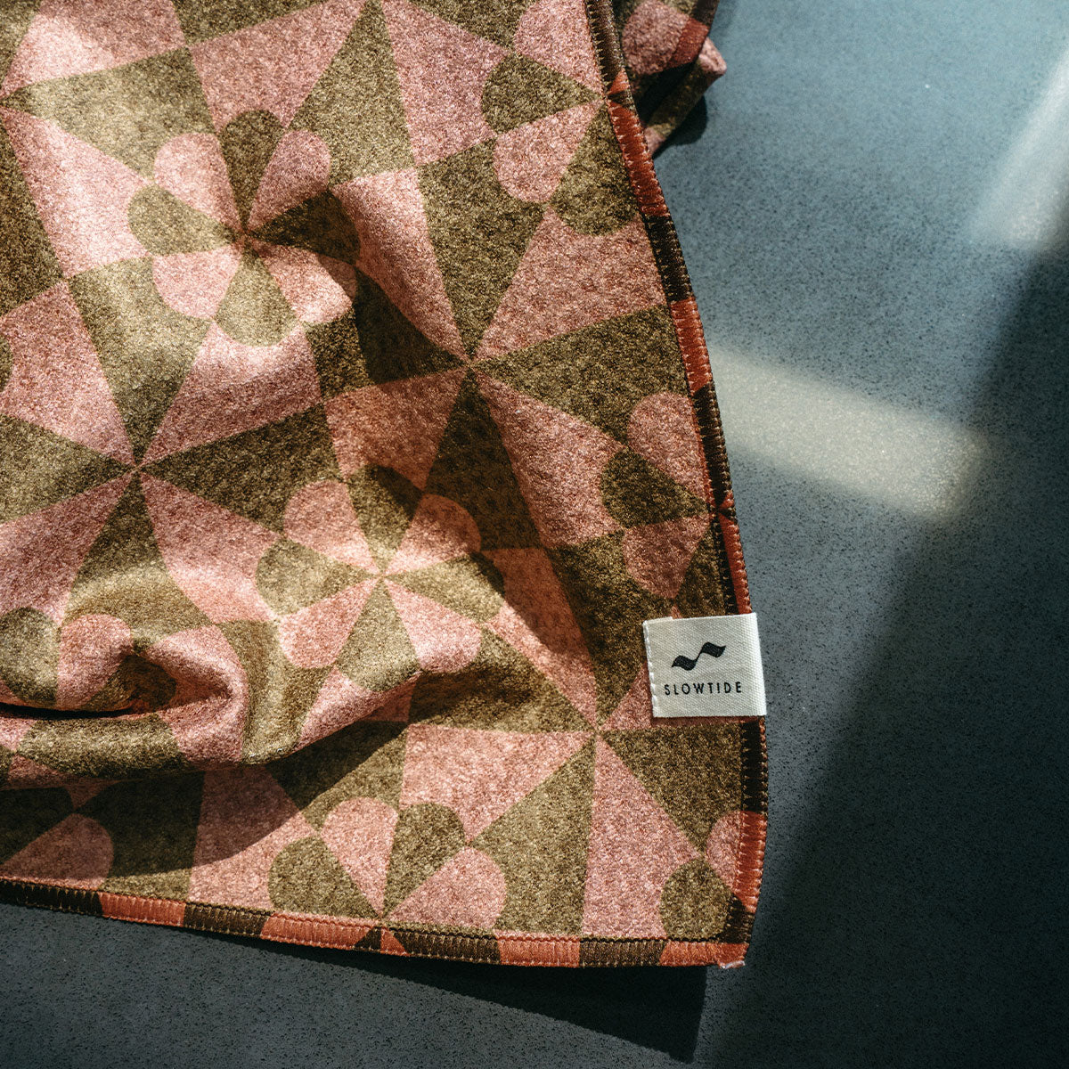 Patchwork blanket with quilt-inspired design on gray surface in sunlight.