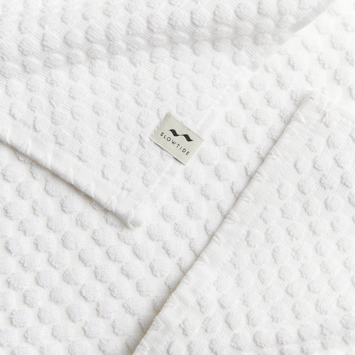 Spa towel, white textured cotton with sustainable material tag.