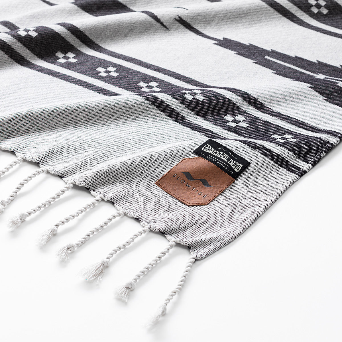 Picnic blanket with black geometric patterns, white fringe, and two corner labels.