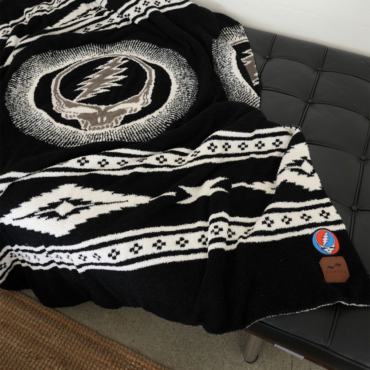 Throw blanket with black and white skull and lightning bolt design on a bench.