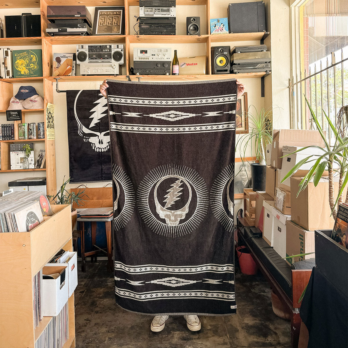 Black woven cotton towel with white lightning skull design in a record store setting.