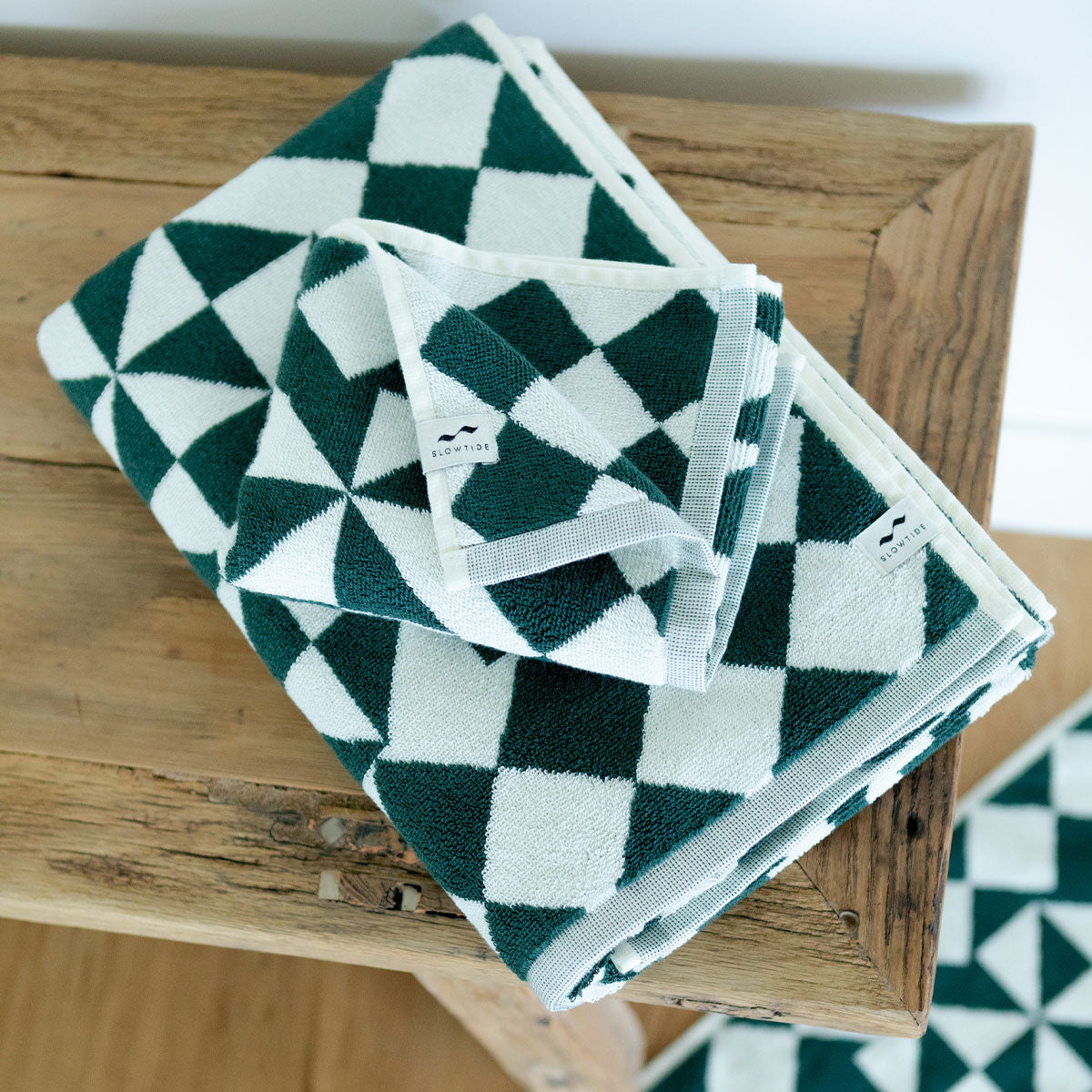 Plush hand towels with a green and white geometric pattern folded on a wooden bench.