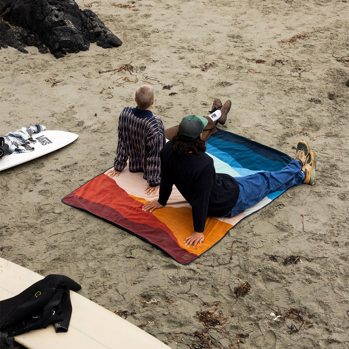 Water-repellent rectangular beach blanket with a multi-colored desert print on sand.