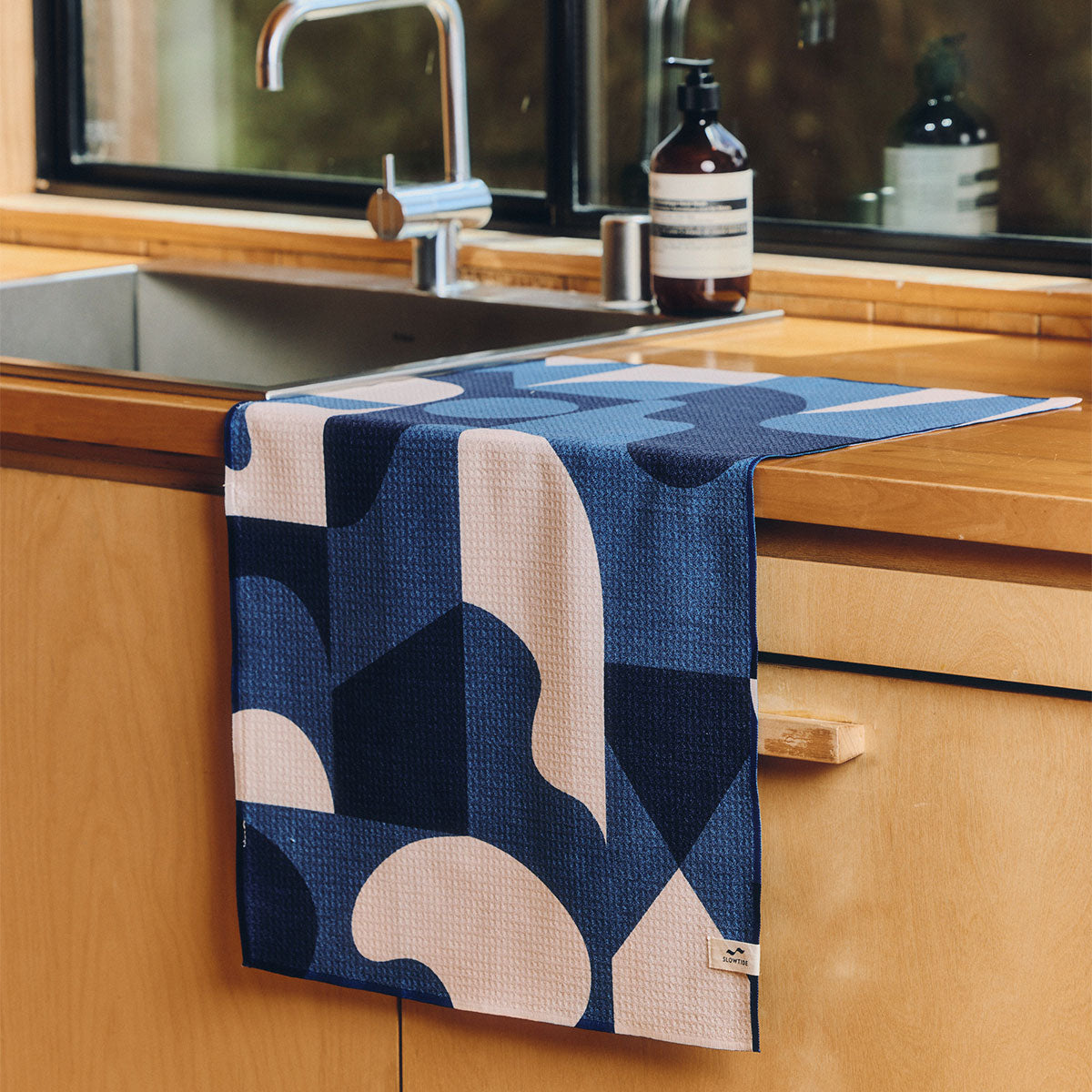 Sustainable kitchen towel featuring a blue and cream geometric pattern on a wooden counter.