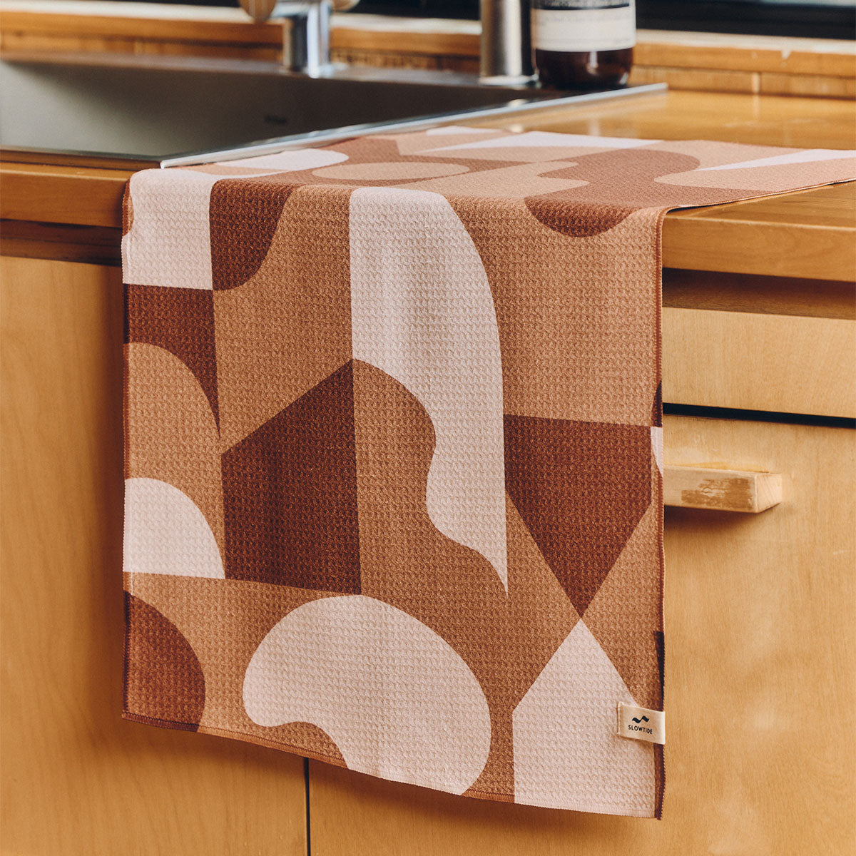 Kitchen towel in waffle-weave with brown and cream geometric pattern on a counter.