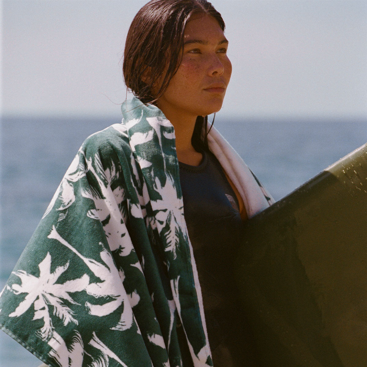Beach towel in sustainable material with a green and white palm print wrapped around a surfboard.